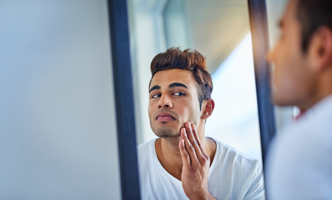 man looking in mirror after Sofwave treatment for acne scars